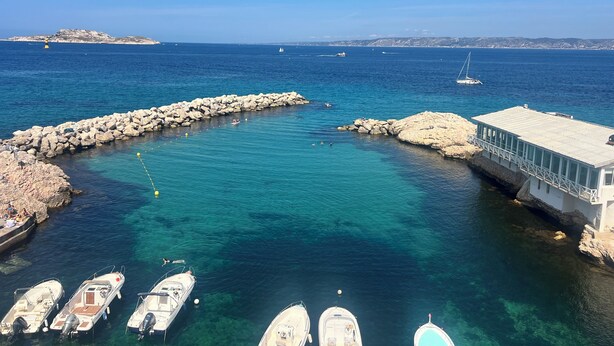 A coastal marina with boats docked, a rocky breakwater, and a building with a metal railing. - Seafront Cabanon, Access Private to the Sea, Corniche Malmousque! (Marseille)