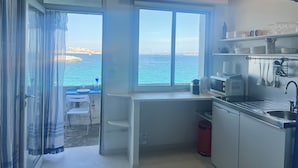 A compact kitchen with a view of the sea, a small dining area, and a red trash bin. - Seafront Cabanon, Access Private to the Sea, Corniche Malmousque! (Marseille)