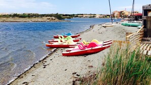 A beach with several colorful paddle boats lined up on the shore, a sandy beach, and a calm body of water.
