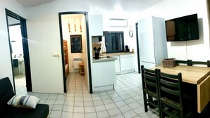 A compact living space with a kitchenette, a dining area with a wooden table and chairs, and a TV mounted on the wall.