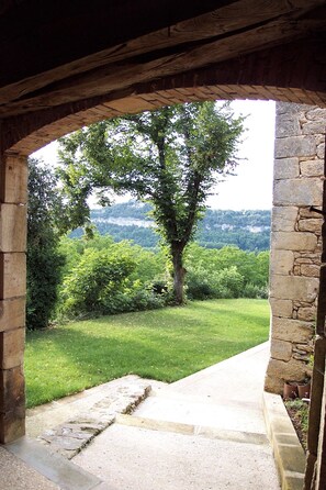 Un arcoado portal de piedra que da a una zona verde con un árbol y vistas de una colina boscosa.