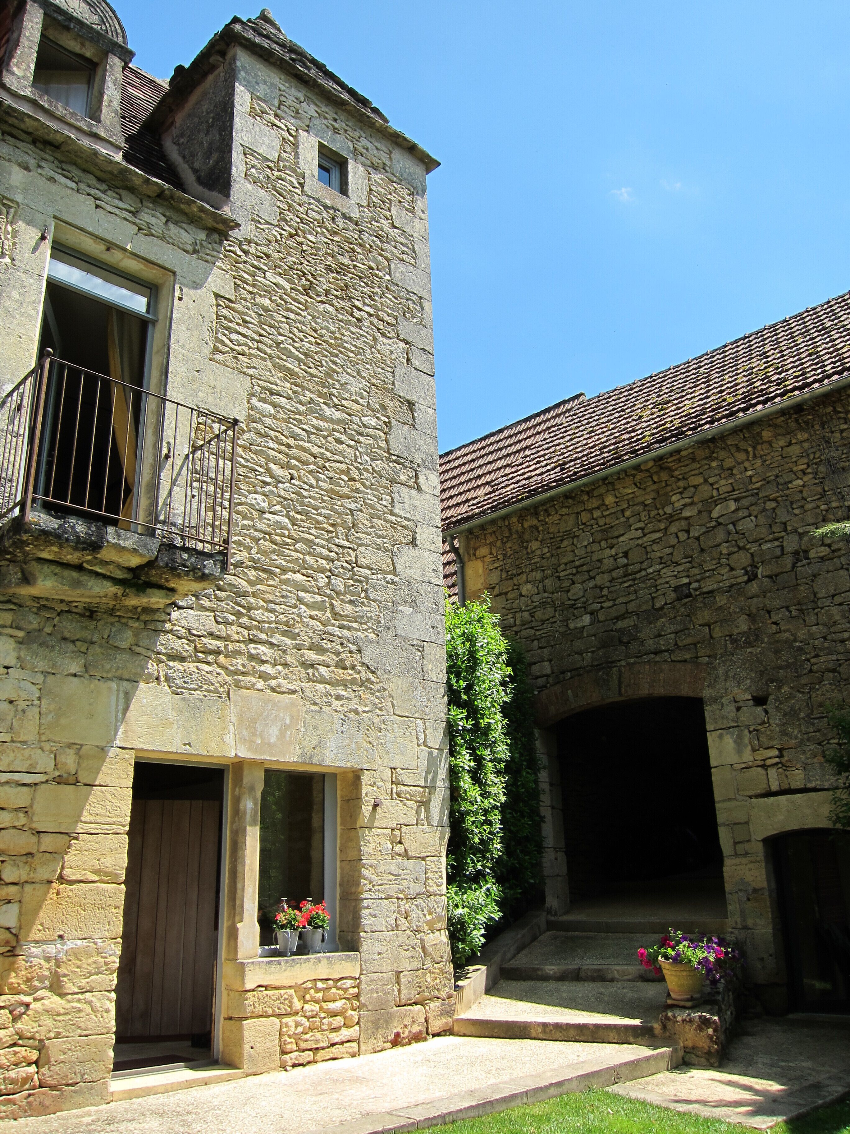 A stone building with a balcony, a door, and a window. There is a potted plant and a flower pot on the ground.