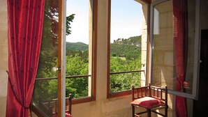 A room with a view of a green landscape through large windows, a wooden chair, and red curtains. - magnificient 16th century MANOR HOUSE with POOL and JACUZZI (Cénac-Et-Saint-Julien)