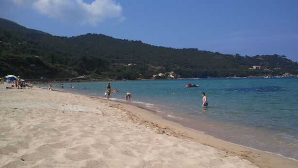 Une plage de sable fin avec une eau cristalline, quelques personnes et un bateau au loin.
