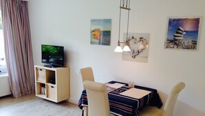 Un comedor con una mesa dispuesta para dos, un televisor sobre un mueble de madera y obras de arte en las paredes.