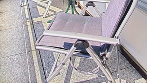 Un balcón con una mesa redonda y cuatro sillas, una pequeña planta en maceta y vistas a un edificio con toldo rojo.