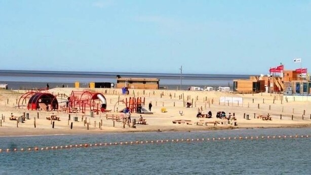 Una playa con una torre de salvavidas, una estructura roja y un edificio con banderas.