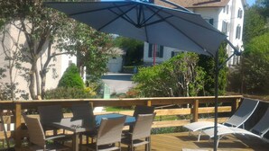 An outdoor deck with a table and chairs, a large umbrella, and a view of a building in the background.