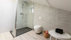 A modern bathroom with a glass-enclosed shower, a white toilet, and a small table with a basket.