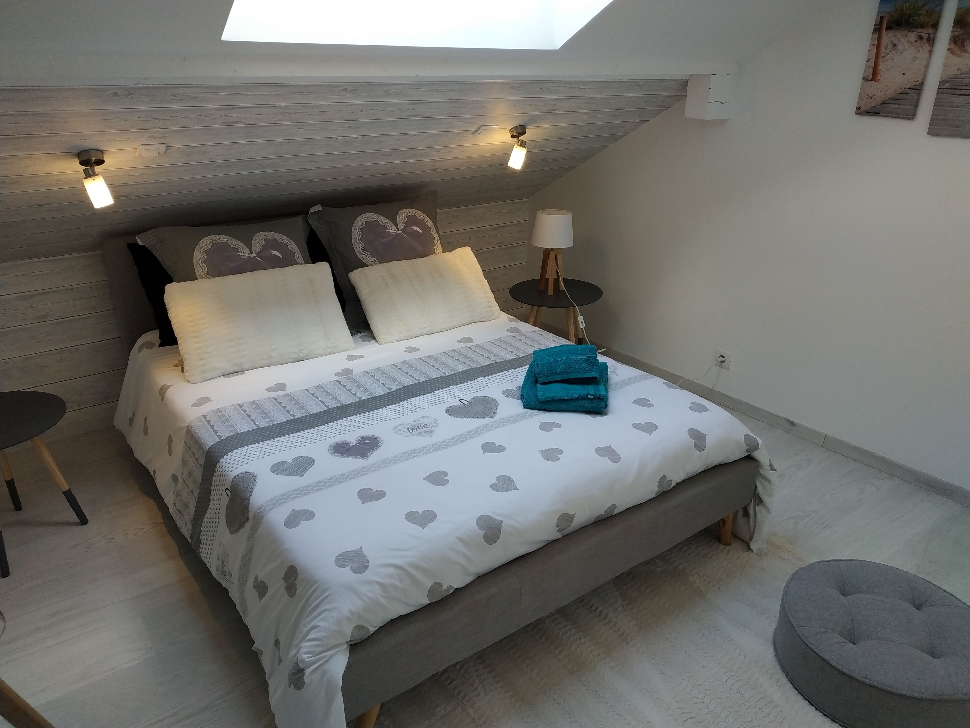 Ein Schlafzimmer mit schrägen Wänden, einem Bett mit Bettwäsche mit Herzmuster, zwei Nachttischlampen und einem kleinen runden Tisch.