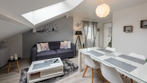 A modern living room with a dark grey sofa, a glass dining table, and a white ceiling with a skylight.
