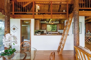 Un interior de madera con zona de comedor, cocina y escalera.