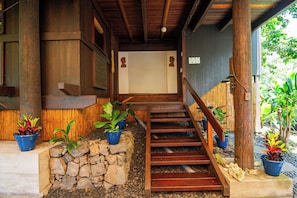 Una escalera de madera lleva a un acceso cubierto con plantas en macetas y un muro de piedra.