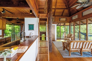 Un interior de madera con una encimera de cocina, una escalera, un sofá y ventanas grandes.