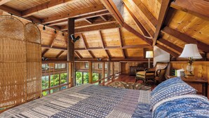 Un intérieur en bois comprenant un lit, une chaise, une lampe et une vue dégagée sur l’extérieur grâce à de grandes fenêtres.