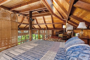 Un interior de madera con una cama, una silla, una lámpara y vistas amplias a través de grandes ventanales.