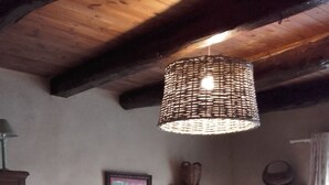 Una sala de estar acogedora con un sofá, reposapiés y una mesa de centro de madera. Hay un televisor sobre un mueble bajo y una lámpara de mimbre colgando del techo.