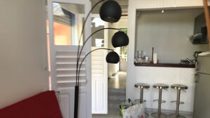 Moderni olohuone, jossa on punainen sohva, musta lattiavalaisin sekä keittiöalue, jossa on baarituoli ja jääkaappi.