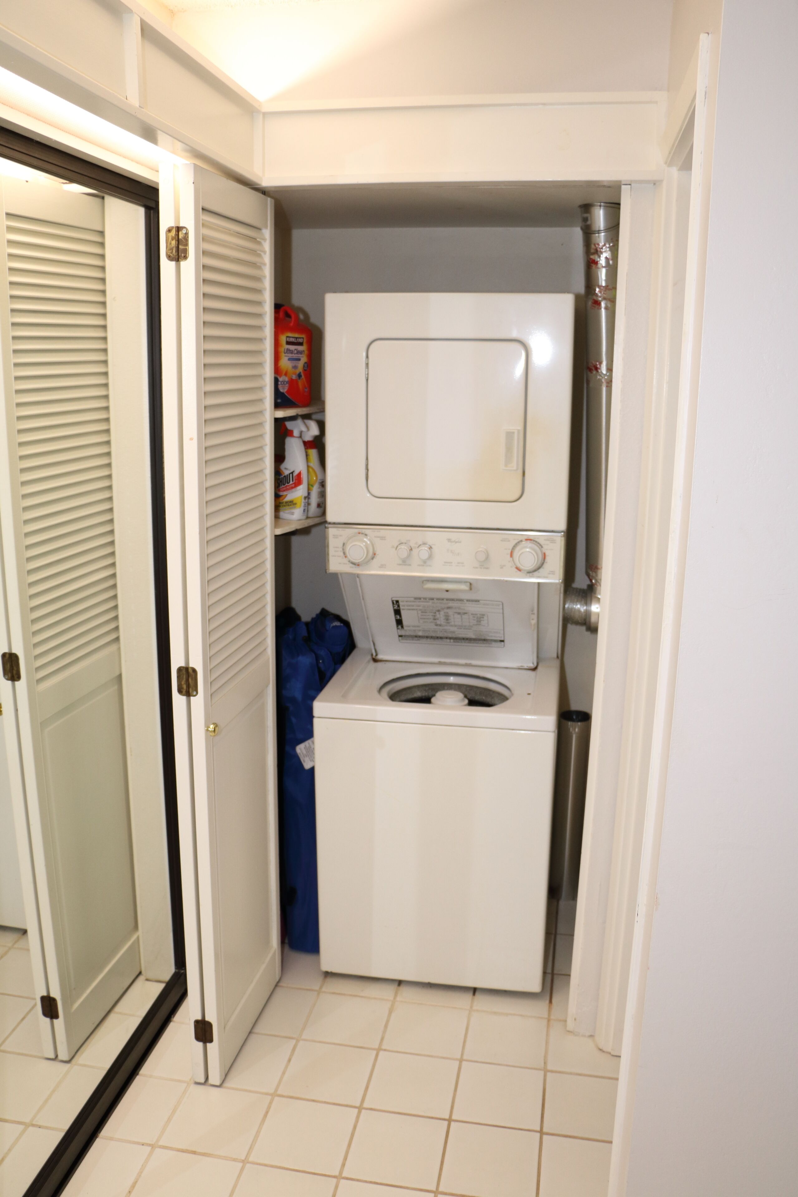A compact laundry room with a washer and dryer, a shelf with cleaning supplies, and a door leading to another room.