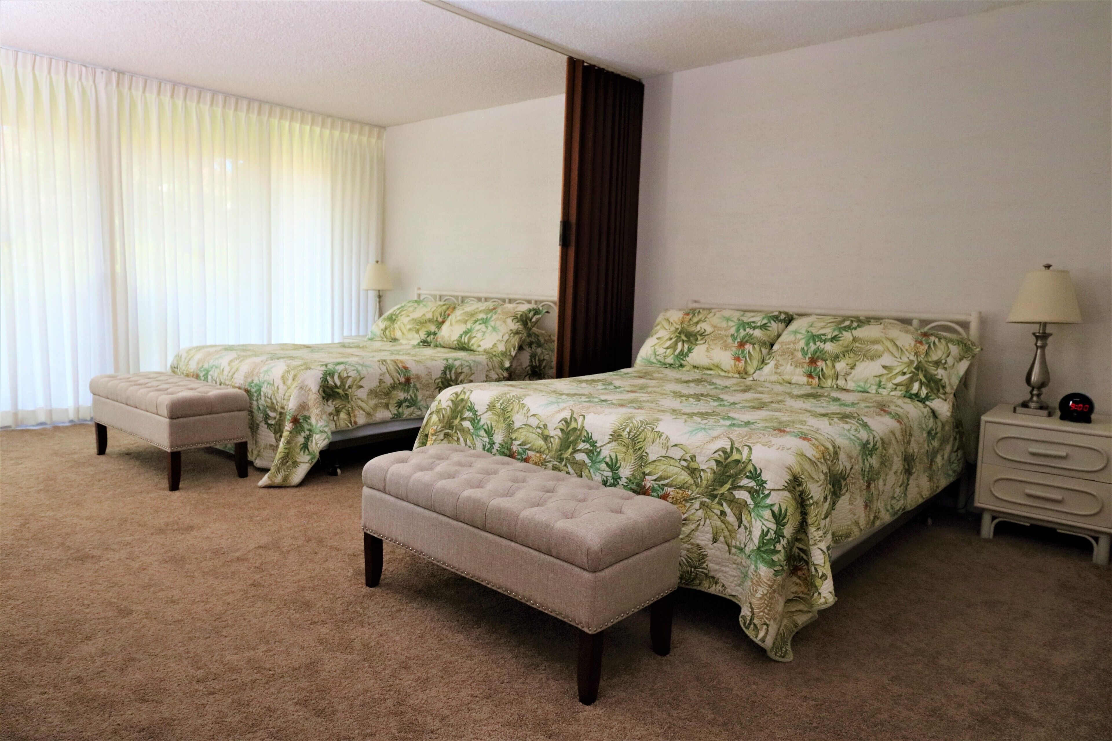 A hotel room with two beds, a bench, a nightstand, and a lamp.