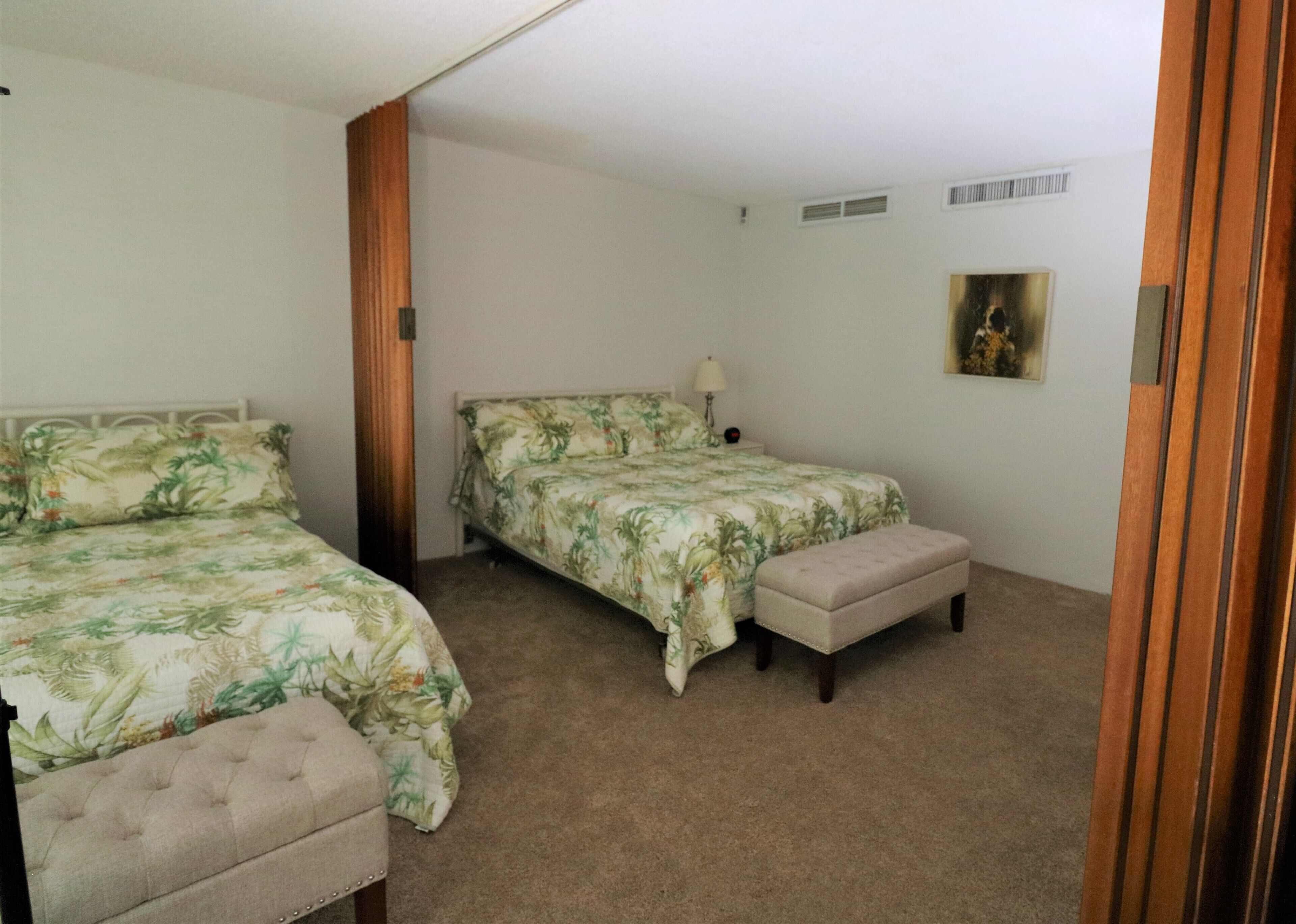 A bedroom with two beds, a bench, and a painting on the wall.