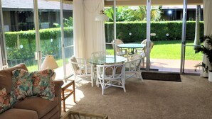 A room with a glass door leading to a garden, a round table with chairs, a sofa with a floral throw, and a lamp. - Maui Eldorado Beachfront Resort - Apt I-101 - Two Bedroom Vacation Rental Condo (Lahaina)
