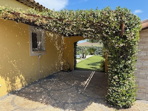Un patio abrité avec un mur jaune, une fenêtre et une vue sur une pelouse verdoyante.