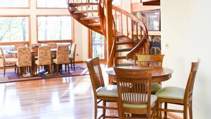 A spacious dining area with a wooden dining table and chairs, a spiral staircase, and large windows offering views of the outdoors.