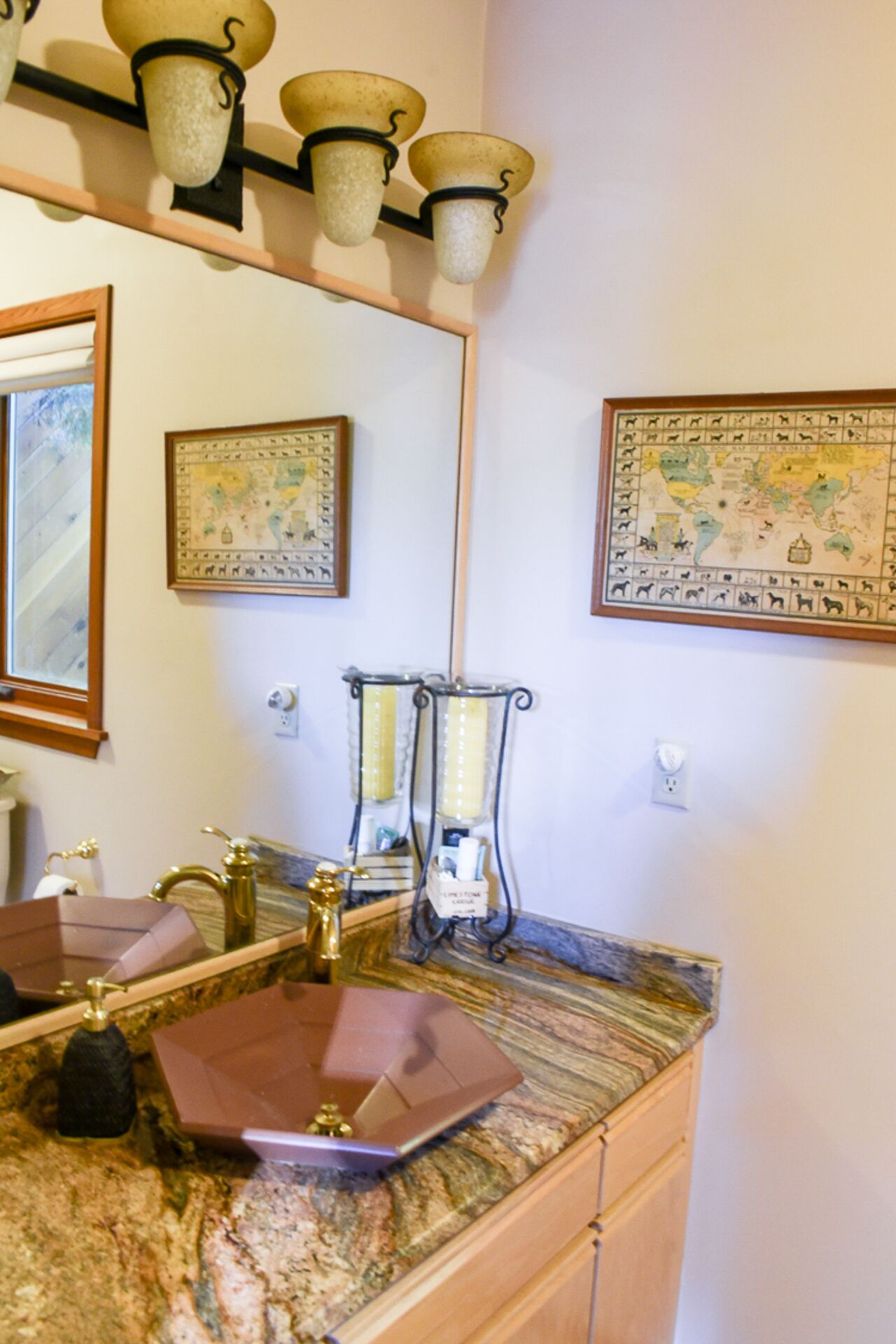 A bathroom with a marble countertop, a gold faucet, a large mirror, and two wall-mounted light fixtures.