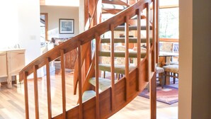 A wooden spiral staircase in a well-lit room with wooden floors and a view of a dining area.