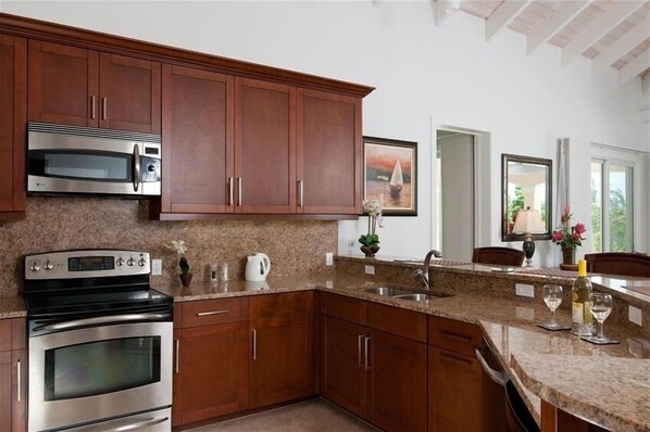 A modern kitchen with granite countertops, stainless steel appliances, and wooden cabinets. - Villa Vivace - New Luxurious Seaside Home (Providenciales)