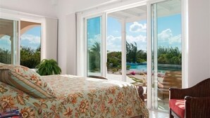 Ein Schlafzimmer mit einem Bett, einem großen Fenster und Blick auf einen Pool und Grünflächen.