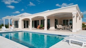 Ein modernes Haus mit Swimmingpool, überdachter Terrasse und Gartenmöbeln.