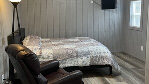 A bedroom with a bed, a ceiling fan, a TV mounted on the wall, and a window. - Cozy 2BR Retreat Near Hurley-Ironwood – Trails, Skiing, Snomobiling (Montreal)