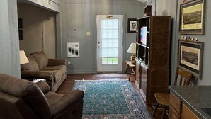 A living room with a brown leather sofa, a blue patterned rug, a wooden bookshelf, and a dining table with chairs. - Cozy 2BR Retreat Near Hurley-Ironwood – Trails, Skiing, Snomobiling (Montreal)