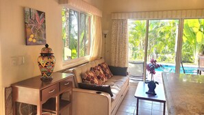 A living room with a sofa, a coffee table, a decorative vase, and a painting on the wall. - Secluded 2 bedroom duplex with private pool and gorgeous jungle and ocean views! (El Divisadero)