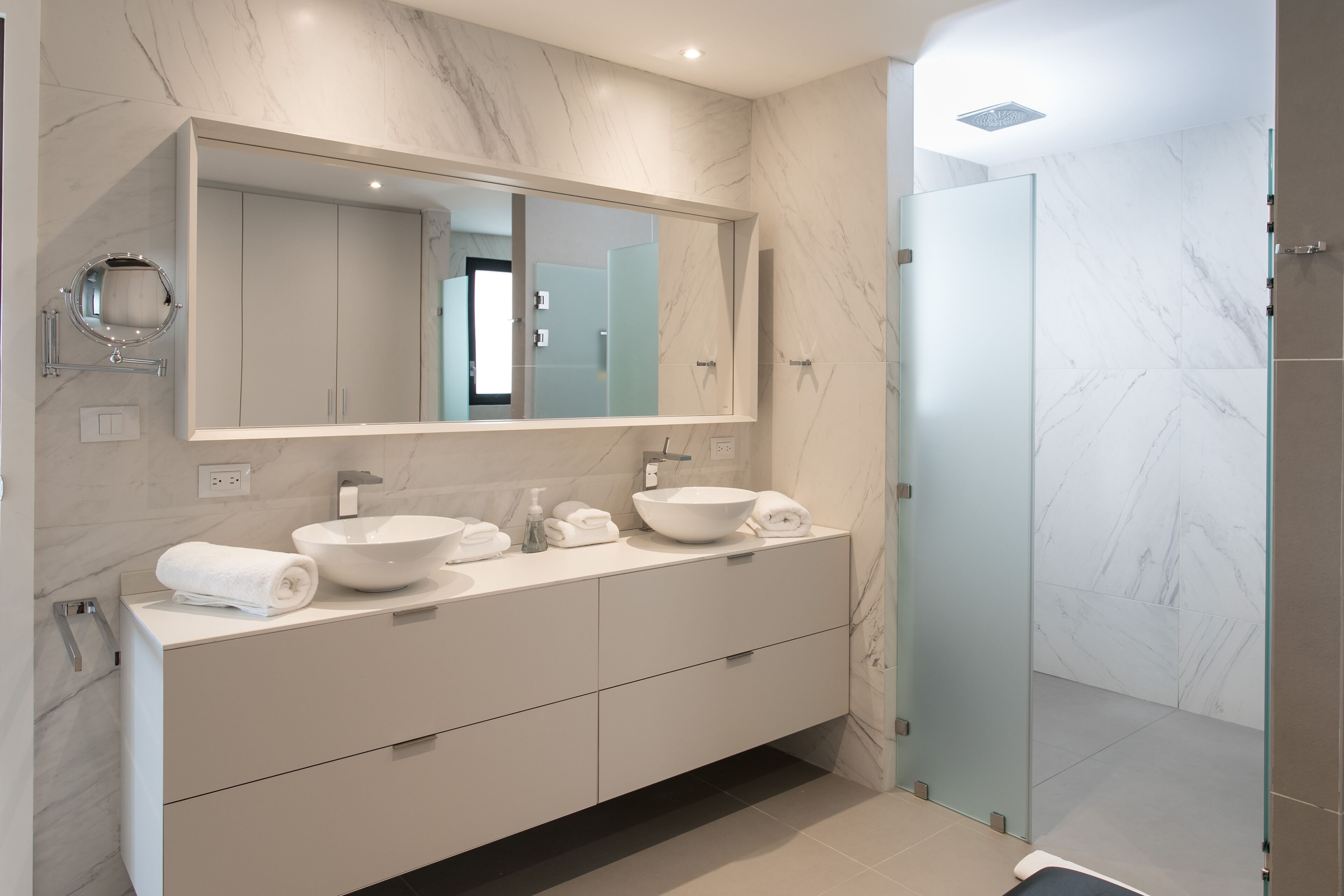 A modern bathroom with a large mirror, two sinks, and a walk-in shower.
