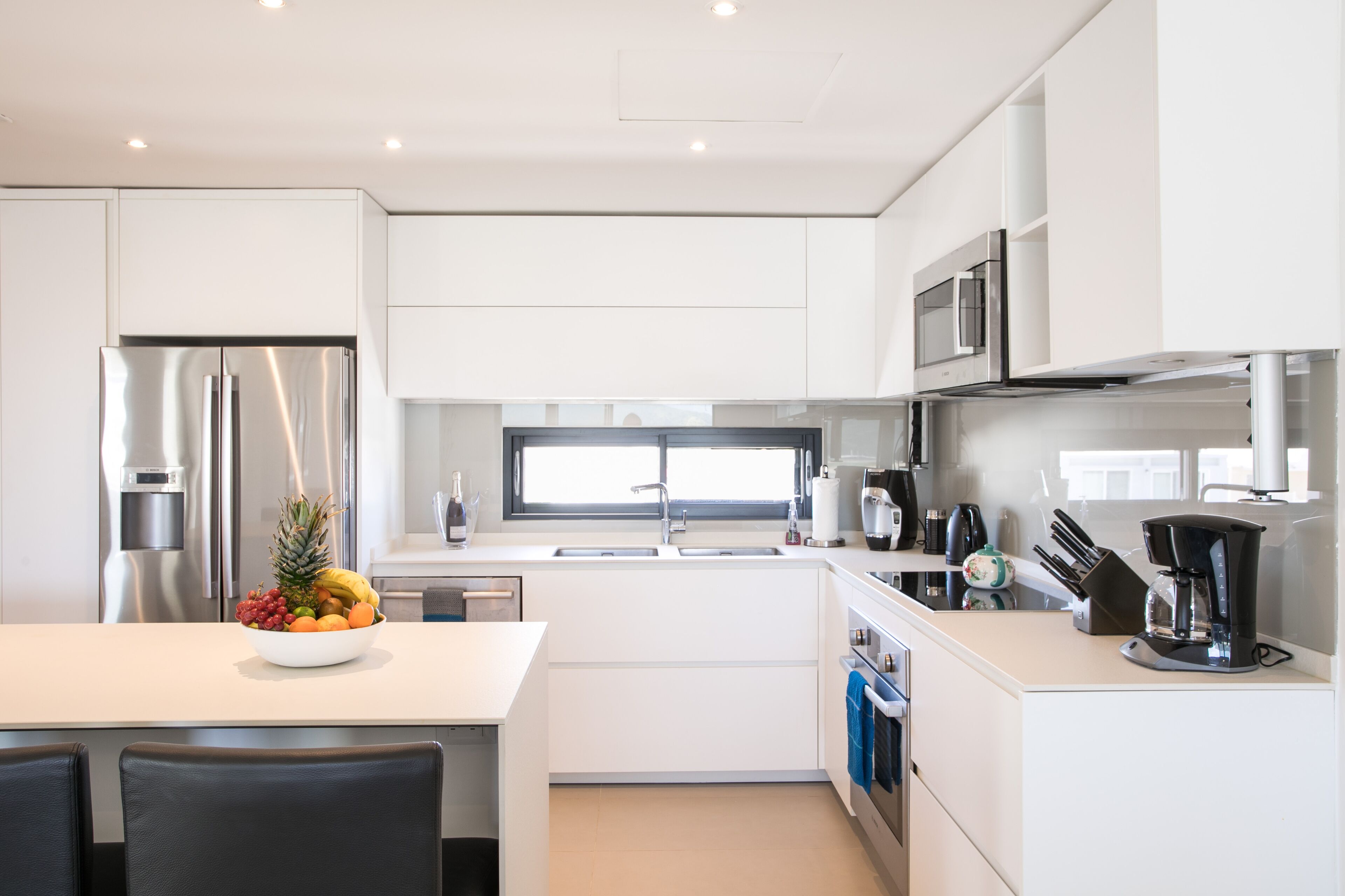 A modern kitchen with white cabinetry, stainless steel appliances, a fruit bowl on the counter, and a coffee maker.