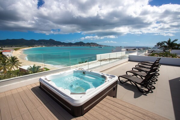 Una azotea con jacuzzi, sillas de descanso y vistas a la playa y las montañas.