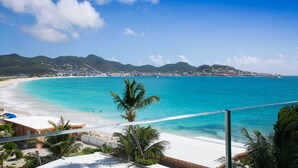 A beach with clear turquoise water, a white sandy shore, and a view of a coastal town in the distance. - OCEAN FRONT 3 BEDROOM PENTHOUSE UNIT. STAY IN LUXURY. (Beacon Hill,)