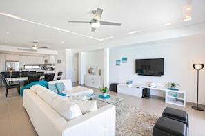 Una sala de estar moderna con un sofá blanco, una mesa de centro de cristal, un televisor de pantalla plana y un ventilador de techo.