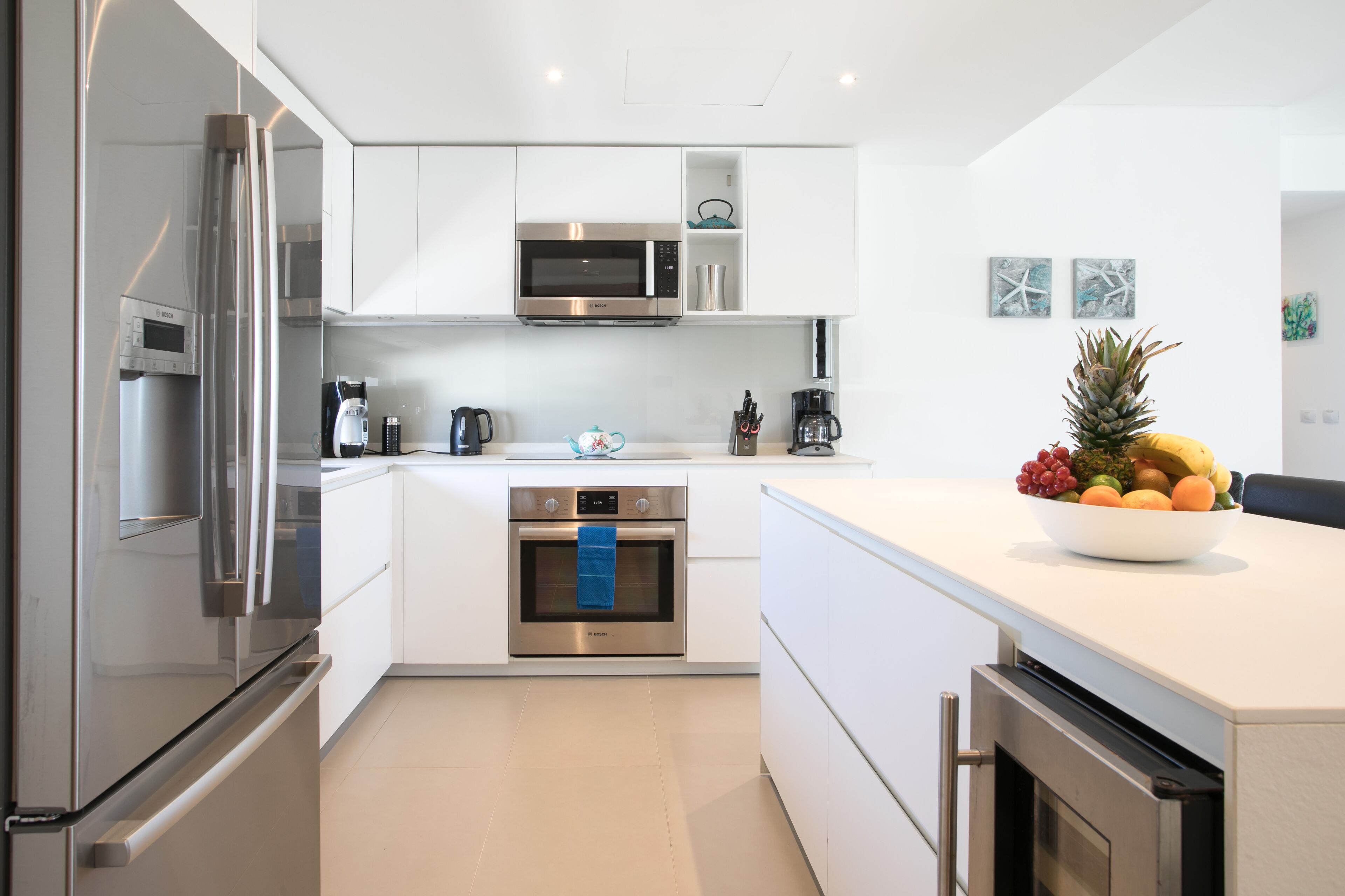 A modern kitchen with stainless steel appliances, white cabinetry, and a fruit bowl on the counter.