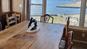 Un coin repas avec une table et des chaises en bois, une vue sur la mer à travers de grandes fenêtres et une plage visible au loin.