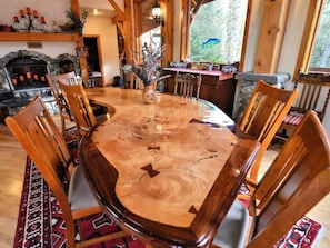 A wooden dining table with chairs, a vase with flowers, and a stone fireplace. - Carriage House - Tecumseh's timber frame Cottage (Anchorage)