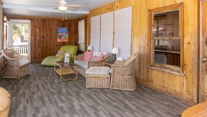 A cozy room with wicker furniture, a ceiling fan, and a large window. - The Gulls Nest Beach House (Edisto Island)