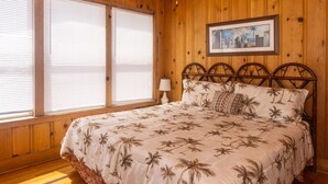 A wooden-paneled room with a bed, large windows, and a framed picture on the wall. - The Gulls Nest Beach House (Edisto Island)