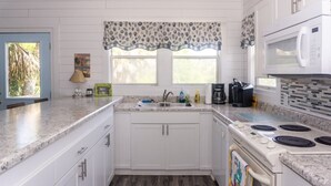 A kitchen with white cabinets, a granite countertop, a microwave, a stove, and a window with a patterned valance. - The Gulls Nest Beach House (Edisto Island)