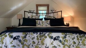 A bedroom with a sloped ceiling, a bed with a floral bedspread, two bedside lamps, and a window with blinds. - Red Poppy- Beautiful home 3 blocks from Elk Ave (Crested Butte)