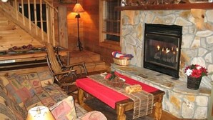 A cozy cabin interior with a stone fireplace, wooden furniture, and a staircase. - Peaceful Real Log Cabin Rushing Trout Stream  Jacuzzi Hot Tub (deep gap)