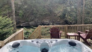 A hot tub on a wooden deck with a view of a forest and a river. - Peaceful Real Log Cabin Rushing Trout Stream  Jacuzzi Hot Tub (deep gap)